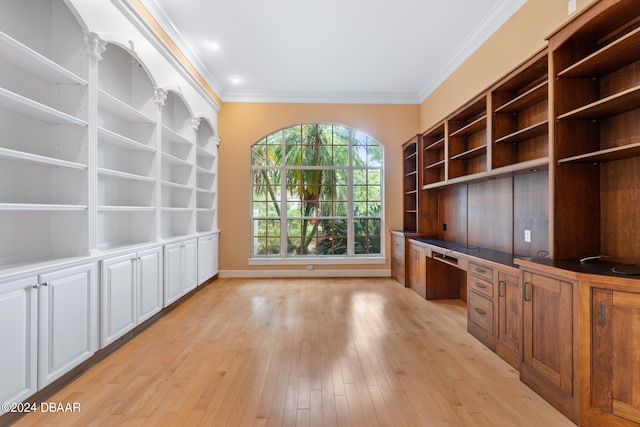 unfurnished office featuring light hardwood / wood-style floors, built in desk, and crown molding