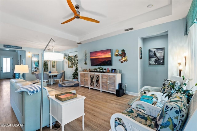 living room with light wood-type flooring, a tray ceiling, and ceiling fan