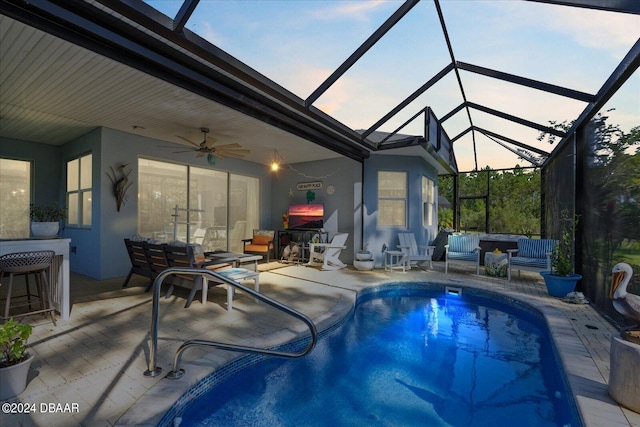 pool at dusk with a patio area, ceiling fan, glass enclosure, and an outdoor living space