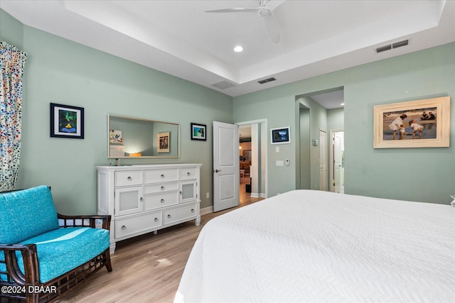 bedroom with a raised ceiling, ceiling fan, and light hardwood / wood-style flooring