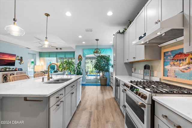 kitchen with sink, light stone countertops, an island with sink, light hardwood / wood-style flooring, and stainless steel stove