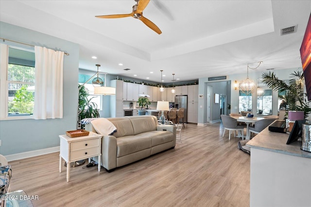 living room featuring ceiling fan with notable chandelier, light hardwood / wood-style flooring, sink, and a tray ceiling