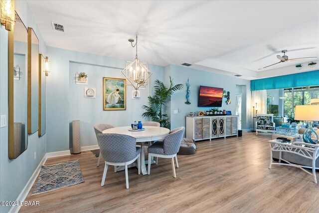 dining space with ceiling fan with notable chandelier and light hardwood / wood-style flooring