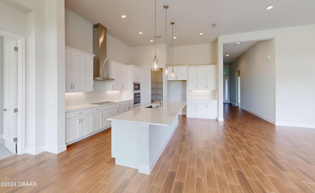 kitchen featuring white cabinetry, sink, wall chimney range hood, a large island with sink, and oven