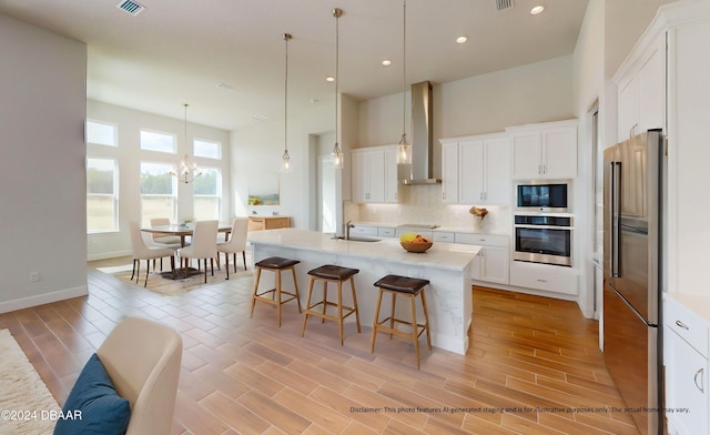 kitchen with appliances with stainless steel finishes, white cabinetry, a kitchen island with sink, and wall chimney exhaust hood