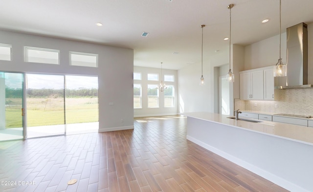 kitchen featuring white cabinets, wall chimney exhaust hood, pendant lighting, and light wood-type flooring