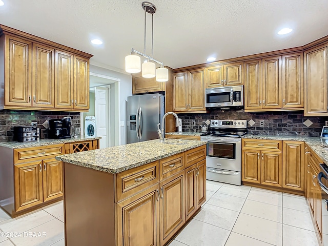 kitchen featuring a kitchen island with sink, stainless steel appliances, light stone counters, and washer / dryer