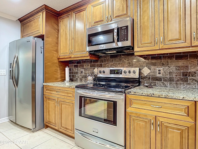 kitchen with light tile patterned flooring, light stone countertops, backsplash, and appliances with stainless steel finishes