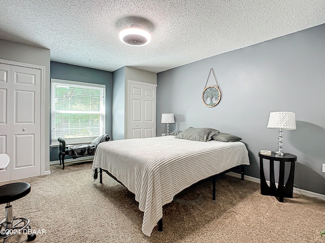 bedroom with a textured ceiling, carpet flooring, and multiple closets