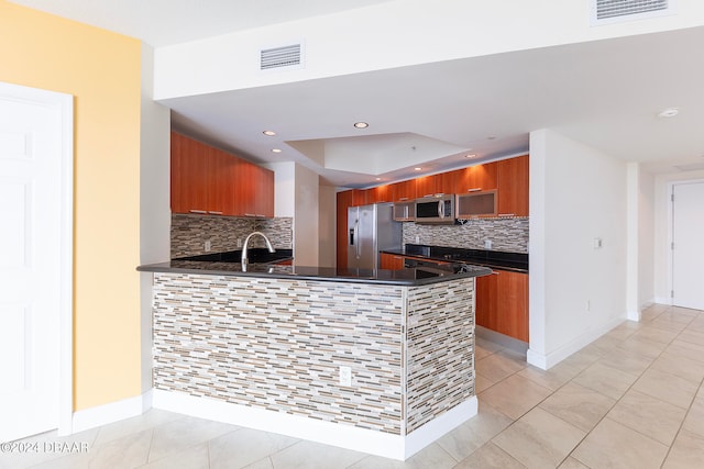 kitchen with tasteful backsplash, light tile patterned flooring, stainless steel appliances, dark stone countertops, and kitchen peninsula