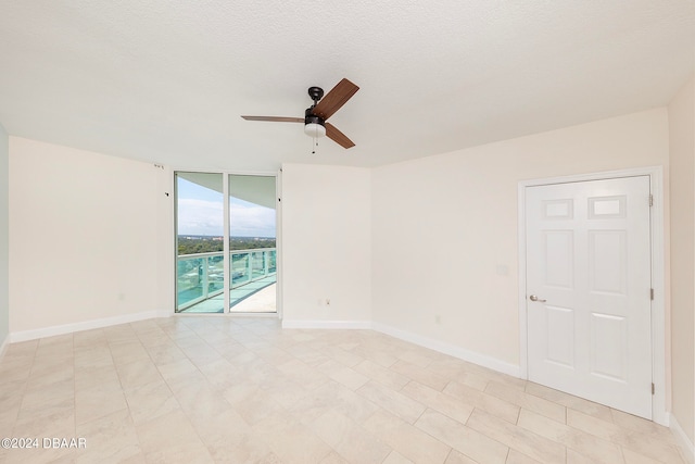 empty room with expansive windows, ceiling fan, and a textured ceiling