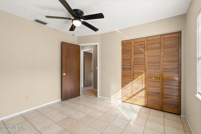 unfurnished bedroom featuring ceiling fan, light tile patterned floors, a textured ceiling, and a closet