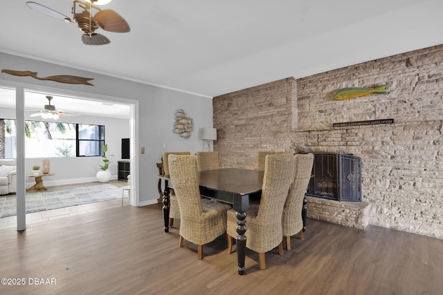 dining room featuring wood-type flooring, a brick fireplace, ornamental molding, and ceiling fan