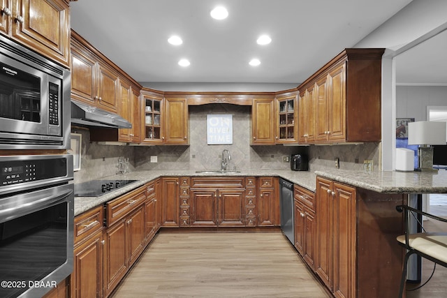 kitchen featuring appliances with stainless steel finishes, sink, kitchen peninsula, light stone countertops, and light wood-type flooring