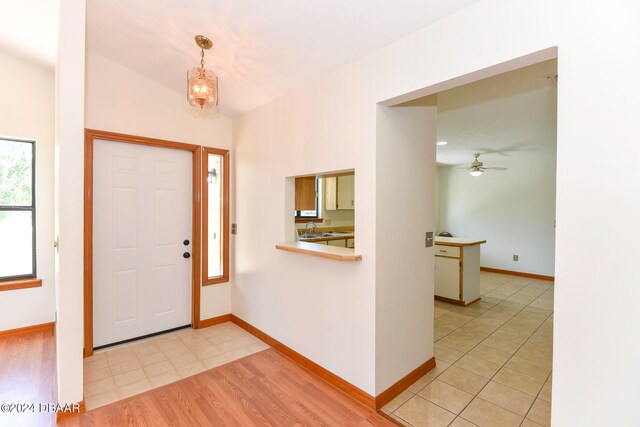 foyer with ceiling fan with notable chandelier, sink, light wood-type flooring, and lofted ceiling