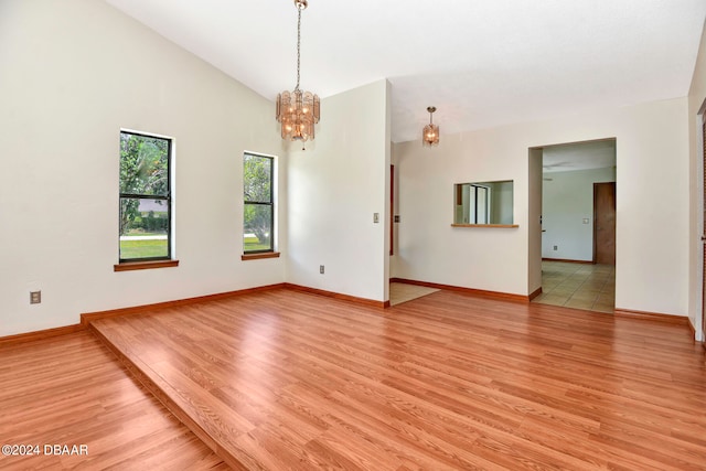 unfurnished room with light wood-type flooring, vaulted ceiling, and a notable chandelier