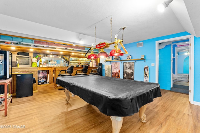 game room with bar, a textured ceiling, light hardwood / wood-style floors, and billiards