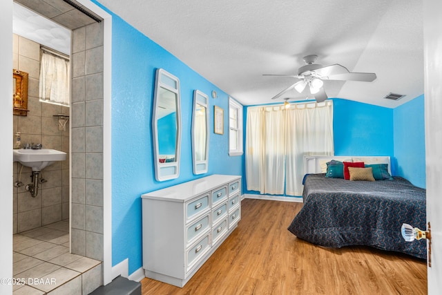 bedroom featuring ceiling fan, ensuite bathroom, a textured ceiling, and light wood-type flooring