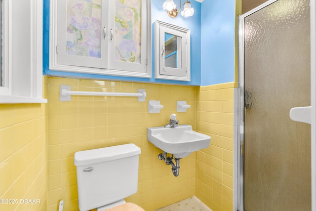 bathroom featuring a shower with door, sink, tile walls, and toilet