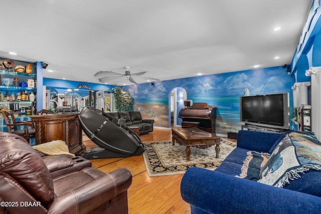 living room with a ceiling fan, wood finished floors, recessed lighting, arched walkways, and indoor bar