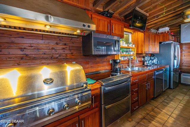 kitchen with exhaust hood, wood walls, appliances with stainless steel finishes, and a sink