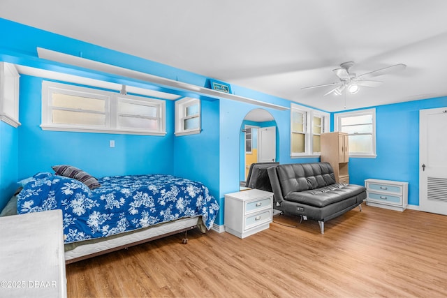 bedroom with a ceiling fan, wood finished floors, and arched walkways