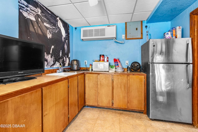 kitchen with white microwave, a wall mounted air conditioner, electric panel, freestanding refrigerator, and a paneled ceiling