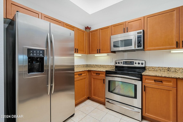 kitchen with light tile patterned flooring, light stone countertops, stainless steel appliances, and tasteful backsplash