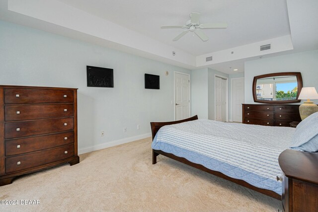 carpeted bedroom with ceiling fan, a raised ceiling, and a closet