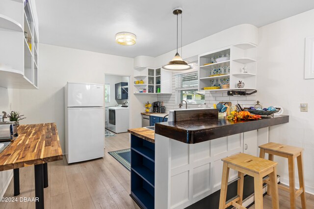 kitchen featuring hanging light fixtures, wood counters, light hardwood / wood-style flooring, washer / clothes dryer, and white fridge