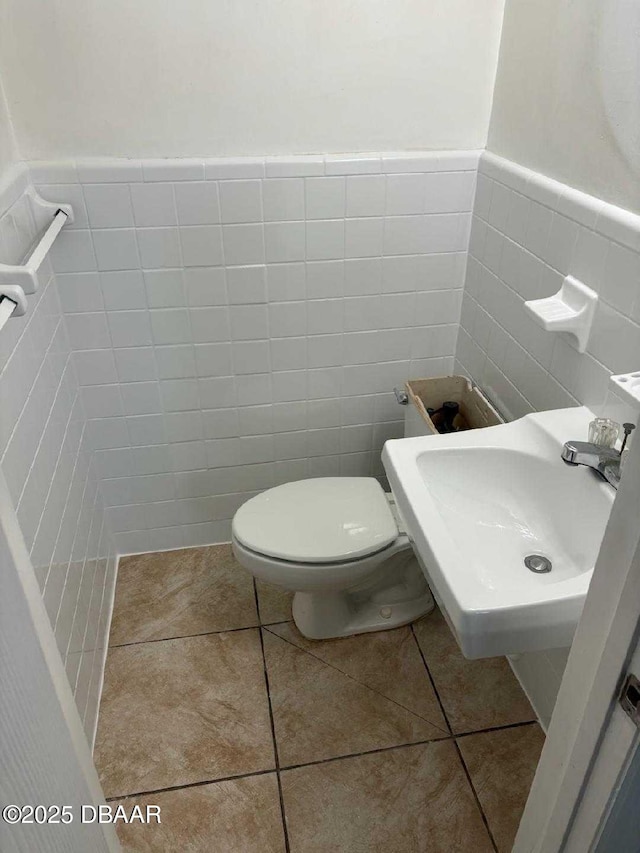 bathroom with tile patterned floors, toilet, sink, and tile walls