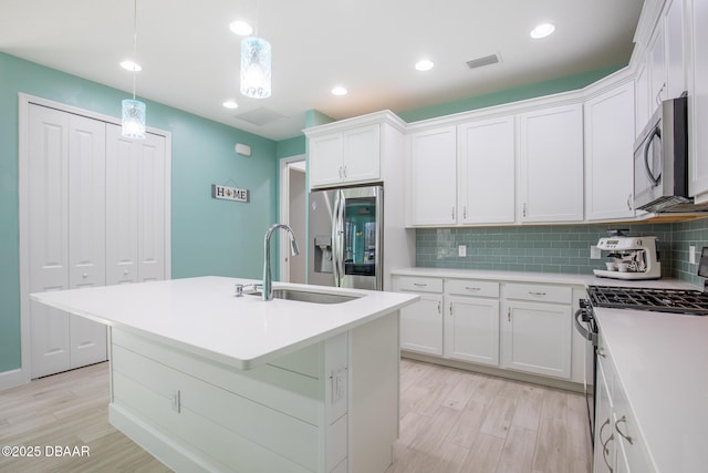 kitchen with stainless steel appliances, an island with sink, hanging light fixtures, and white cabinets