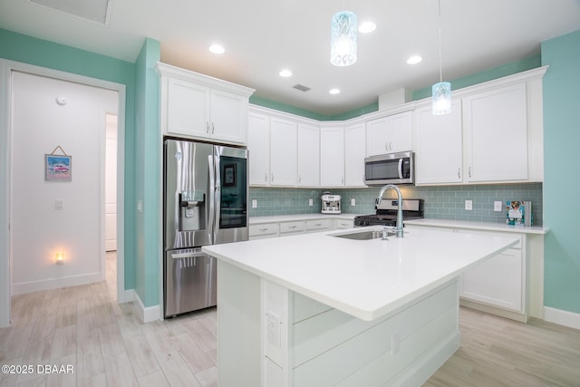 kitchen featuring stainless steel appliances, a center island with sink, white cabinets, and decorative light fixtures