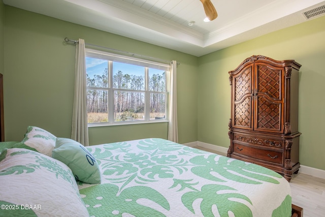 bedroom with ceiling fan, ornamental molding, light hardwood / wood-style floors, and a tray ceiling