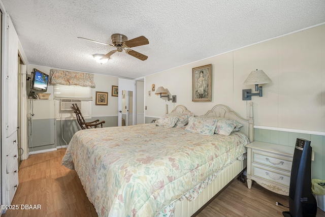 bedroom with a ceiling fan, a textured ceiling, wood finished floors, and a wainscoted wall