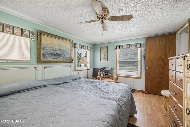 bedroom with radiator heating unit, a textured ceiling, ceiling fan, and light wood-style flooring