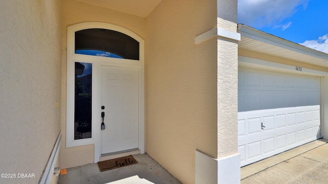 entrance to property with a garage and stucco siding