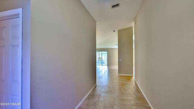 hallway with baseboards, visible vents, and light tile patterned floors