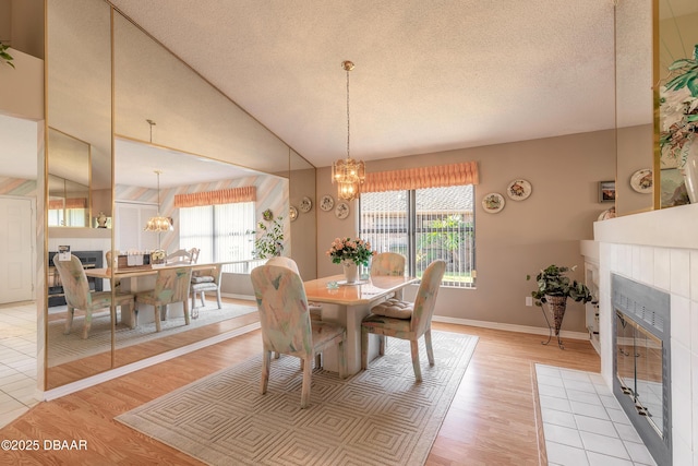 dining area with a healthy amount of sunlight, a tiled fireplace, vaulted ceiling, and light hardwood / wood-style flooring