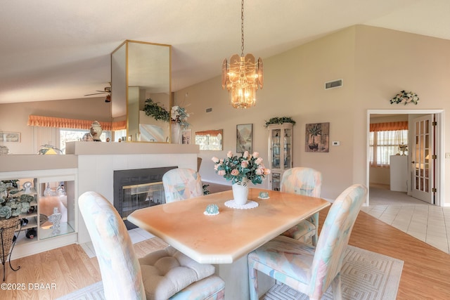 dining room featuring ceiling fan, light wood-type flooring, a fireplace, and high vaulted ceiling