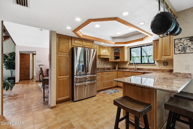 kitchen with a kitchen breakfast bar, kitchen peninsula, a tray ceiling, and stainless steel fridge