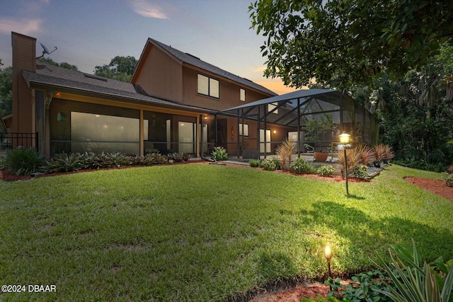 back house at dusk featuring a yard and glass enclosure