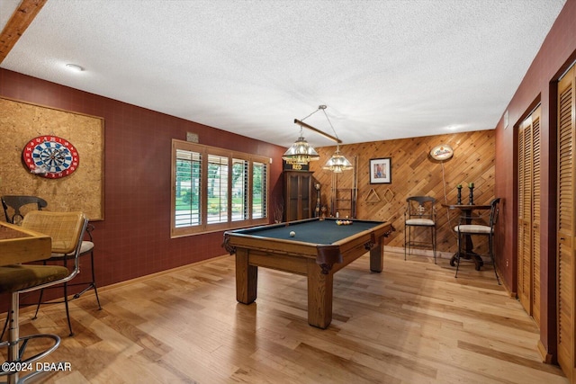 rec room with pool table, light hardwood / wood-style flooring, a textured ceiling, and wooden walls