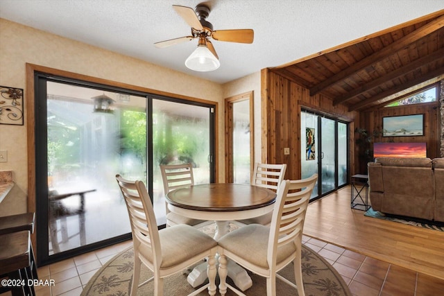 dining room with vaulted ceiling with beams, wood walls, wooden ceiling, ceiling fan, and light hardwood / wood-style flooring