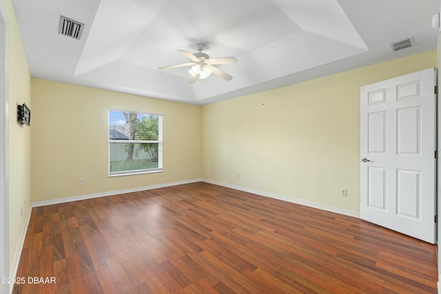 empty room with dark hardwood / wood-style floors, a raised ceiling, and ceiling fan