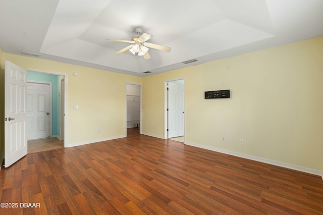 unfurnished bedroom featuring a raised ceiling, ceiling fan, dark wood-type flooring, a spacious closet, and a closet