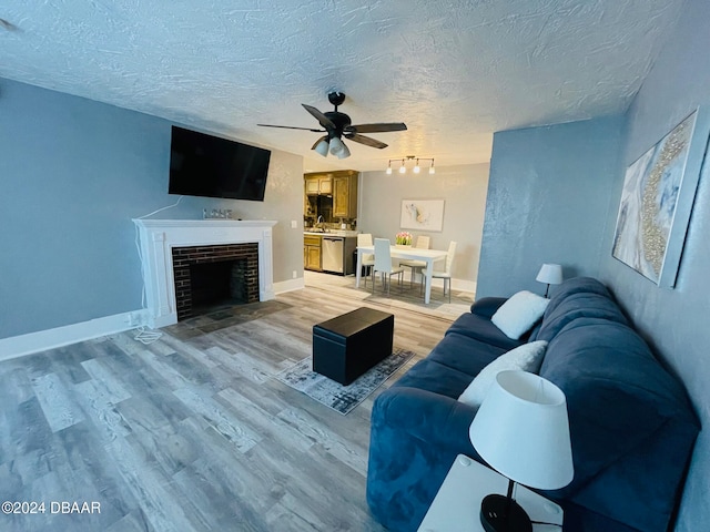 living room featuring a textured ceiling, ceiling fan, a fireplace, and light hardwood / wood-style flooring