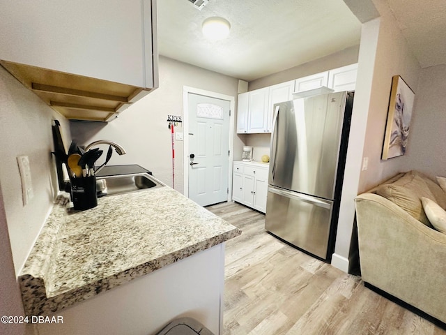 kitchen with light stone countertops, stainless steel fridge, sink, light hardwood / wood-style flooring, and white cabinetry