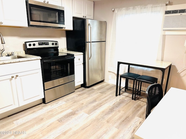 kitchen featuring stainless steel appliances, a wall unit AC, sink, white cabinets, and light hardwood / wood-style floors