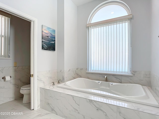 bathroom featuring toilet, plenty of natural light, and a relaxing tiled tub